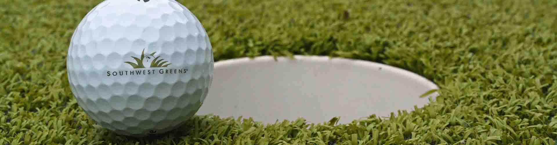 Southwest Greens branded golf ball resting at the edge of a putting cup on artificial turf