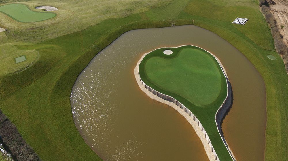 Fresno Aerial view of a vibrant green synthetic grass island in a natural pond on a golf course